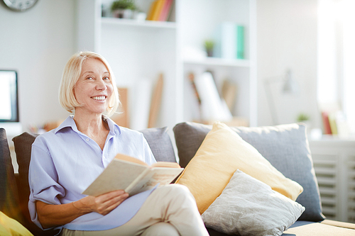 Portrait of contemporary adult woman smiling happily sitting on sofa at home and , copy space