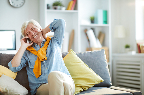 Portrait of contemporary senior man speaking by phone at home and smiling happily, copy space