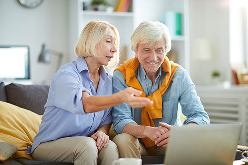 Portrait of contemporary senior couple using laptop together at home and smiling happily, copy space