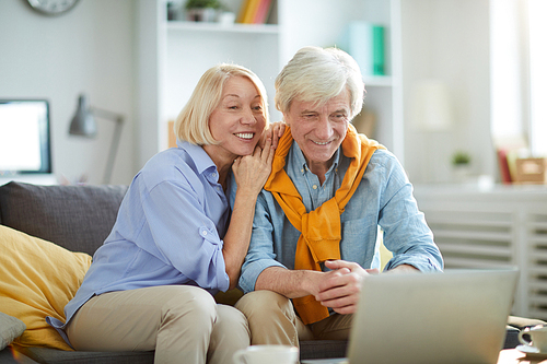 Portrait of contemporary senior couple watching videos sitting on sofa at home, copy space