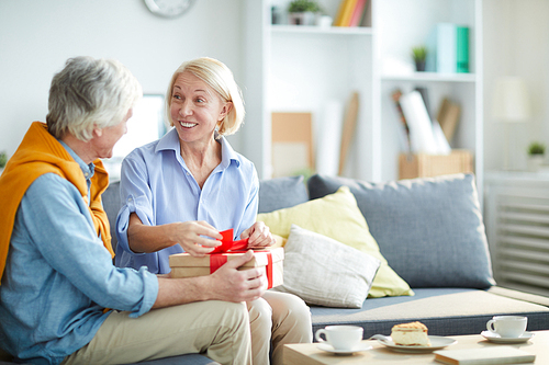 Portrait of contemporary mature couple exchanging gifts at home focus on woman unwrapping gift box, copy space