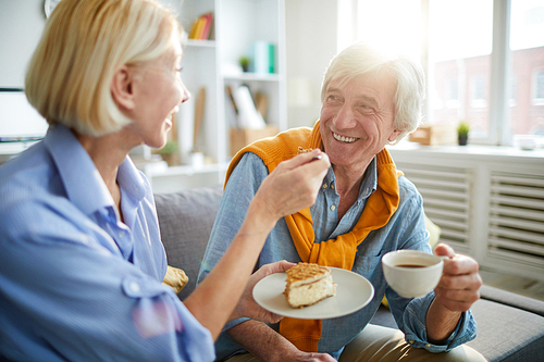 Portrait of happy mature couple enjoying tea and cake in sunlit apartment, copy space