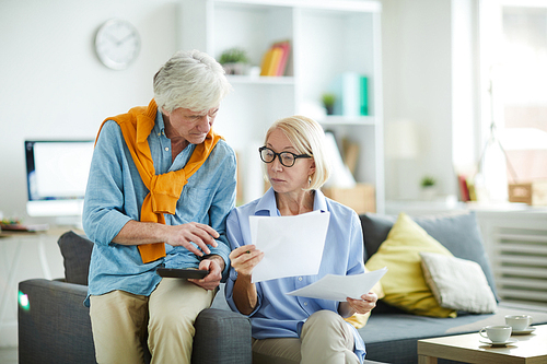 Portrait of contemporary mature couple calculating finances at home holding tax forms, copy space
