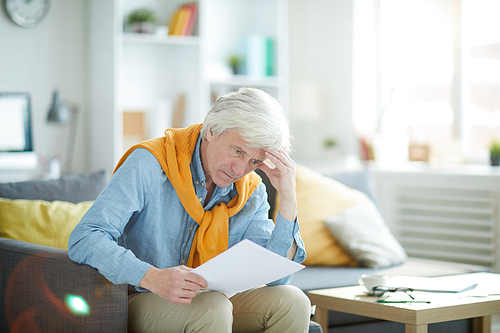 Portrait of frowning mature man looking at financial document, copy space