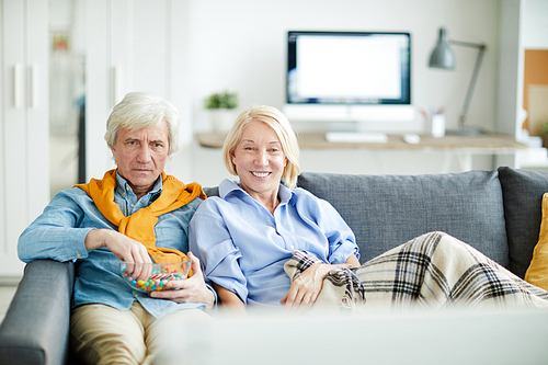 Portrait of contemporary mature couple watching tv together at home sitting on comfortable sofa, copy space