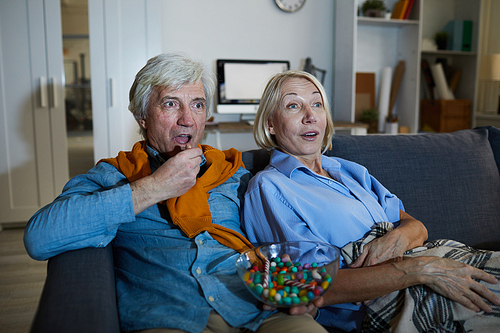 Portrait of contemporary mature couple watching tv in dark sitting on comfortable sofa, copy space
