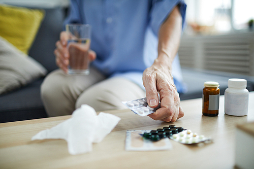 Closeup of unrecognizable senior woman taking pills and medication off table at home, copy space