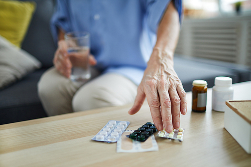 Close up of unrecognizable senior woman taking pills and medication off table at home, copy space
