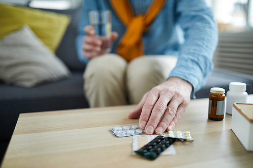 Close up of unrecognizable senior man taking pills and medication off table at home, copy space