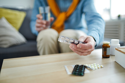 Closeup of unrecognizable senior man taking pills and medication off table at home, copy space