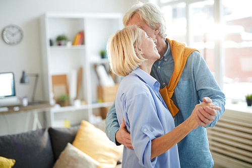 Waist up portrait of happy senior couple dancing at home, copy space