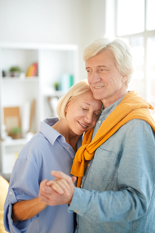 Waist up portrait of happy senior couple dancing at home lit by sunlight