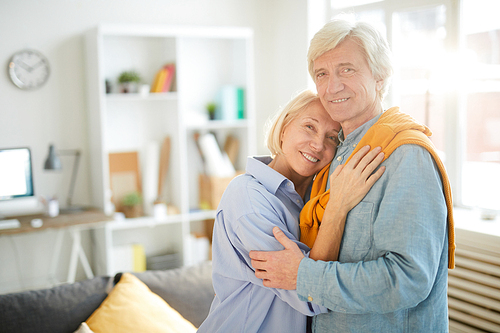 Waist up portrait of happy senior couple embracing tenderly at home and 