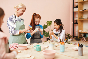 Group of children making handmade ceramics in workshop with mature female teacher, copy space