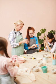 Portrait of children making handmade ceramics in workshop with mature female teacher, copy space