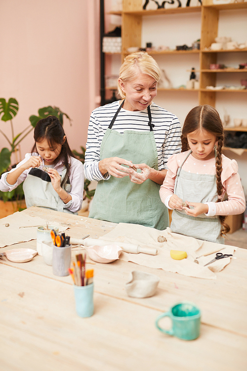 Mature woman making handmade ceramics with two children in pottery class, copy space