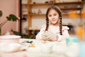 Portrait of cute little girl in pottery class looking at camera and smiling cheerfully, copy space