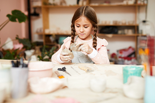 Portrait of cute little girl making handmade ceramics in pottery class, copy space