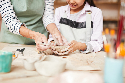 Close up portrait of mother and little girl shaping clay together enjoying pottery class in workshop, copy space