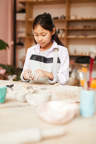 Portrait of Asian girl shaping clay while enjoying pottery class in workshop, copy space
