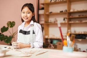 Waist up portrait of Asian girl smiling at camera while enjoying pottery class in workshop, copy space