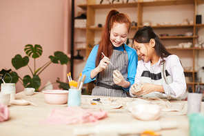 Portrait of two happy girls shaping clay while making handmade ceramics in pottery class, copy space