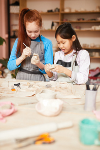 Waist up portrait of two girls shaping clay while making handmade ceramics in pottery class, copy space