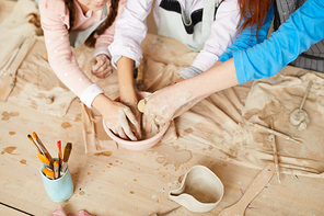 High angle closeup of children making handmade pottery together, putting hands in water bowl, copy space