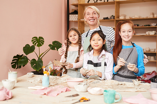 Multi-ethnic group of children posing with teacher in pottery class, copy space