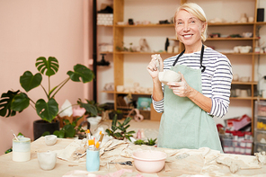 Waist up portrait of smiling female artist  while posing in pottery workshop, copy space