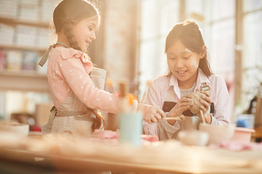 Portrait of two happy girls making handmade pottery in art class lit by sunlight, copy space