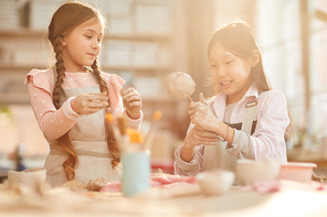 Portrait of two cute girls enjoying pottery in art class lit by sunlight, copy space