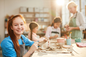 Portrait of smiling teenage girl  while enjoying pottery class with group of children, copy space