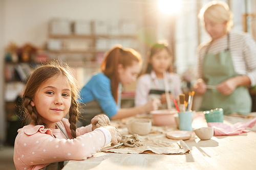 Portrait of cute little girl  while enjoying pottery class with group of children, copy space