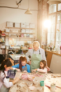 High angle portrait of female art teacher working with children in pottery class, scene lit by serene sunlight, copy space