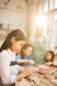 Side view portrait of Asian girl shaping clay in pottery class for children, copy space