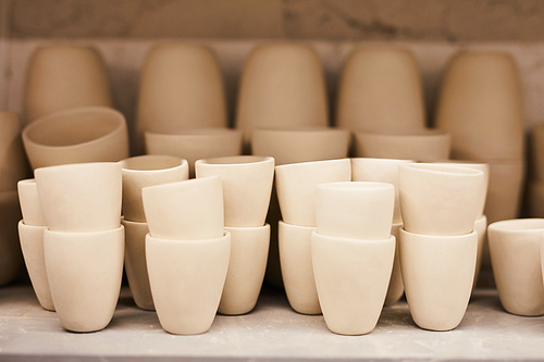Close-up of light beige ceramic mugs without handles stacking on shelf in pottery workshop, background
