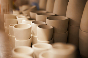 Close-up of beautiful beige ceramic dishware with smooth surfaces place on shelf in pottery workshop