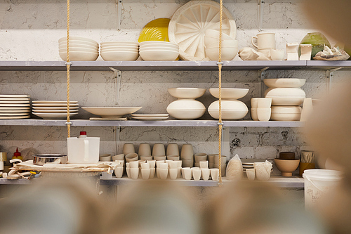 Beautiful creative ceramic dishware of different shapes placed on shelves in store or pottery workshop, copy space