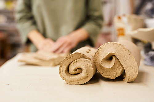 Close-up of rolled soft clay for modelling pot placed on table in workshop, woman preparing clay for moulding