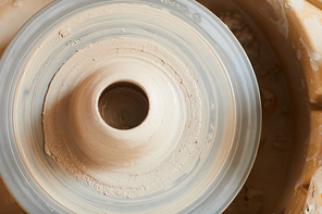 Directly above view of wet soft clay with hole in middle placed on dirty pottery wheel in ceramics studio