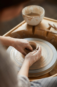 Close-up of unrecognizable woman with smeared hands shaping clay on pottery wheel while making vase with love