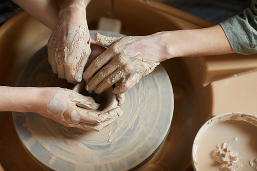 High angle view of unrecognizable women with hands smeared with clay using pottery wheel while moulding vase together