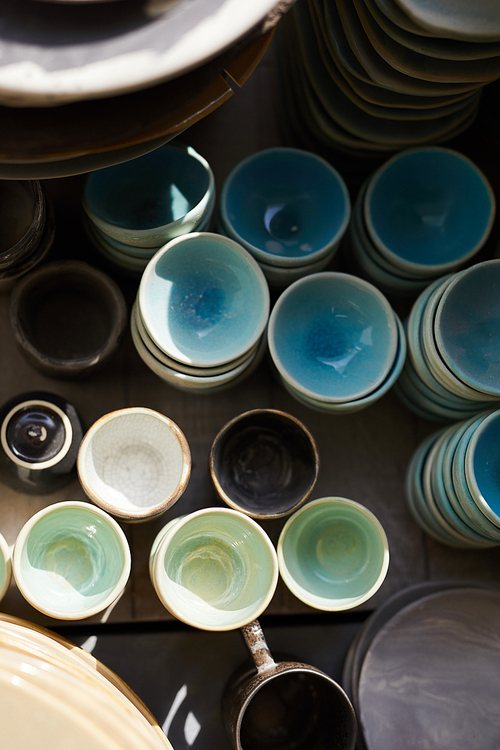 Directly above view of colorful textured bowls stacking on shelf in crockery store or pottery workshop, background