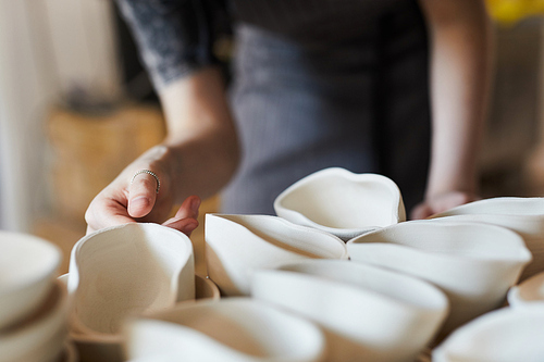 Close-up of unrecognizable woman with ring standing at shelf with ceramic products and choosing ceramic sauce boat in shape of shell of mouth