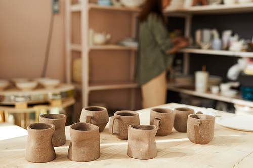 Background image of clay mugs on wooden table table in traditional pottery shop, copy space