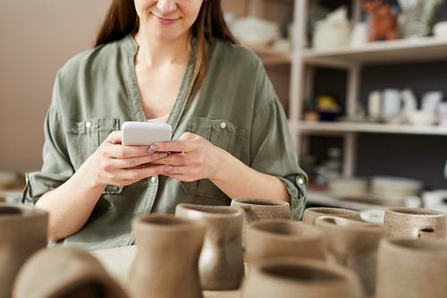 Mid section portrait of contemporary artisn using smartphone while working in pottery shoip, copy space