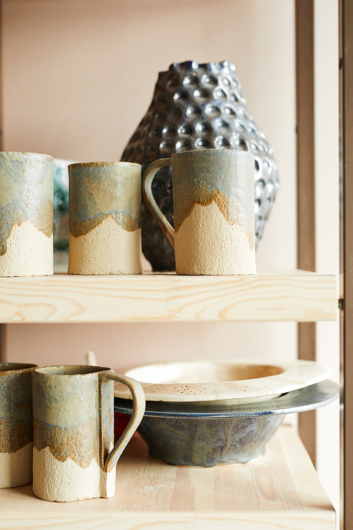 Closeup of rustic cupboard shelf with handmade plates and mugs lit by sunlight, copy space