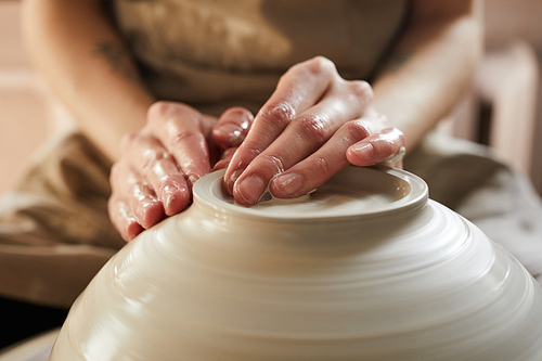 Extreme closeup of unrecognizable female artisan shaping bowl on potters wheel, copy space