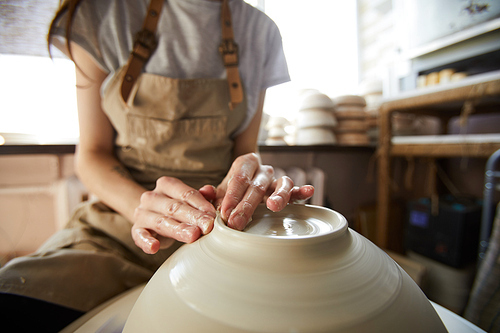 Close up of unrecognizable female artisan shaping bowl on potters wheel, copy space